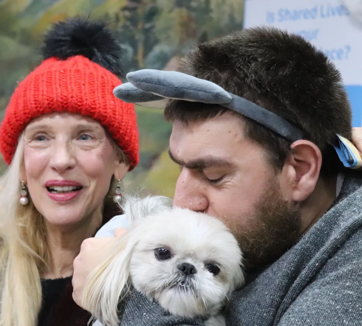 Image of persona Christmas fair. A man and a woman pictures enjoying the fair, the man is cuddling the dog.