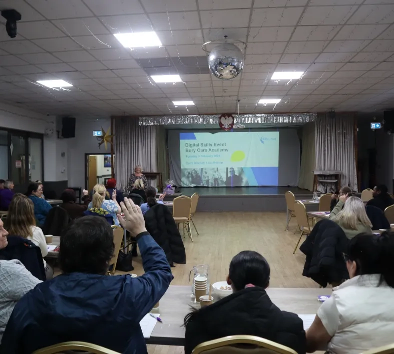 Woman raises hand at Bury Care Academy Digital Skills event, while speaker addresses the room