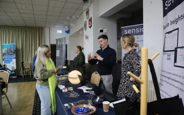 A care provider is stood at a stall at the event speaking to partners about the event.
