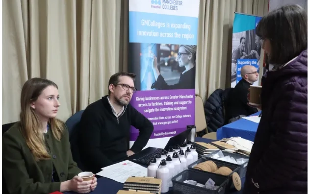 Side angel shot of attendee visiting one of the stalls at the fair as the two people at the stall engage the attendee in conversation